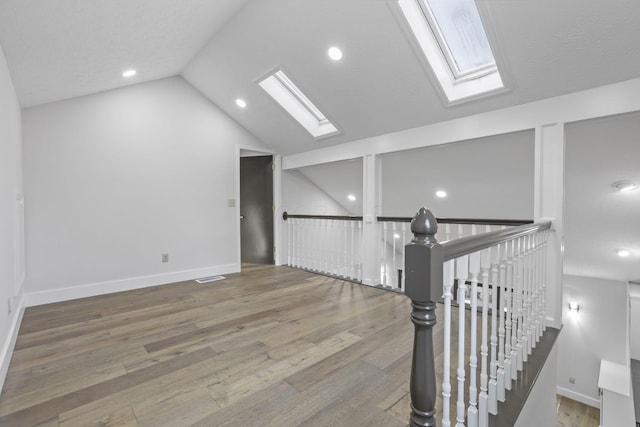 additional living space featuring lofted ceiling with skylight, baseboards, visible vents, and hardwood / wood-style floors