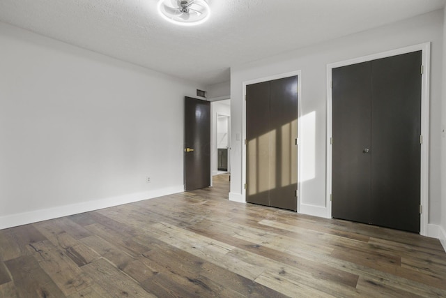 unfurnished bedroom with a textured ceiling, wood-type flooring, visible vents, and baseboards