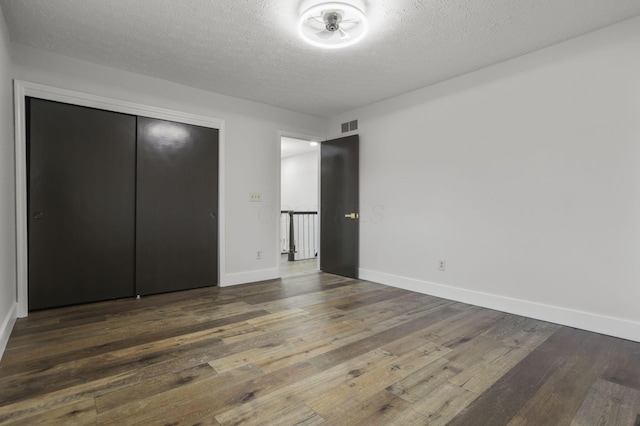 unfurnished bedroom with a textured ceiling, visible vents, baseboards, a closet, and wood-type flooring