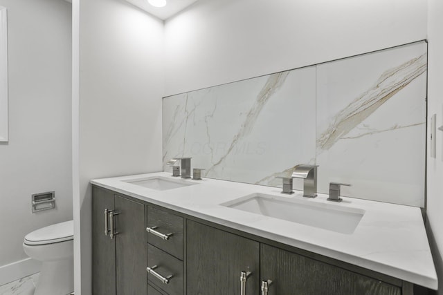 bathroom with marble finish floor, double vanity, a sink, and toilet