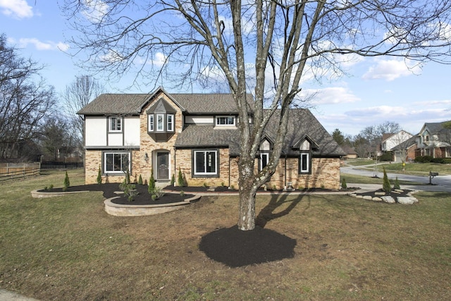 view of front of home featuring a shingled roof, a front yard, brick siding, and fence