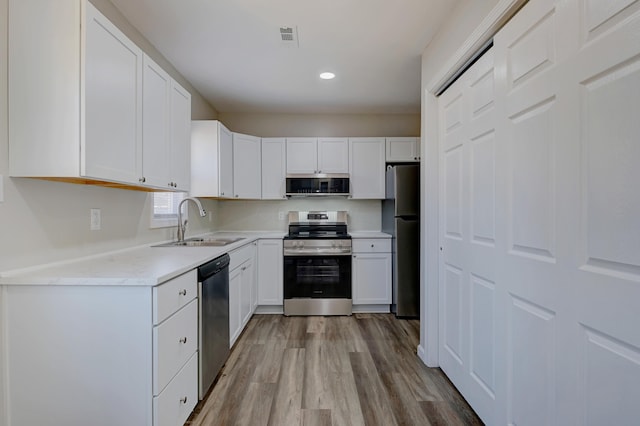 kitchen featuring light wood-style floors, white cabinetry, stainless steel appliances, and a sink