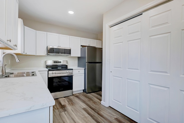 kitchen featuring recessed lighting, appliances with stainless steel finishes, light wood-style floors, white cabinetry, and a sink