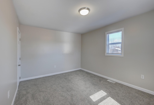 spare room with carpet floors, visible vents, and baseboards