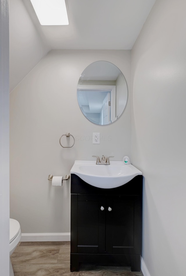 half bath featuring toilet, baseboards, wood finished floors, and vanity