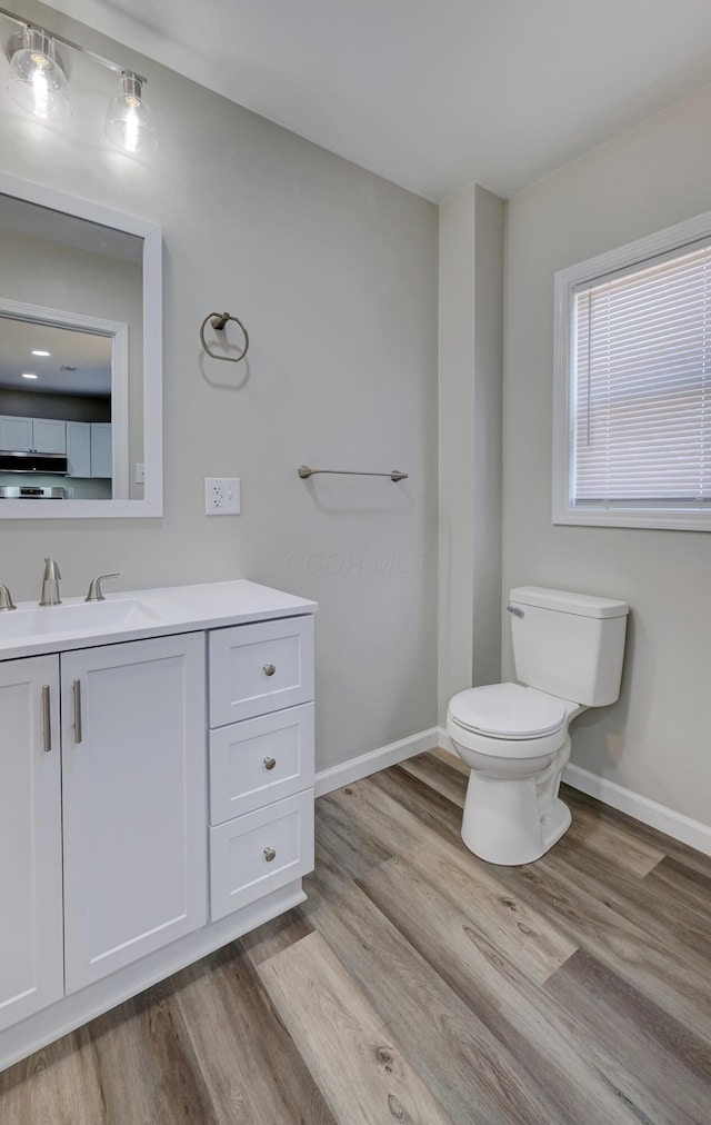 half bathroom featuring baseboards, vanity, toilet, and wood finished floors