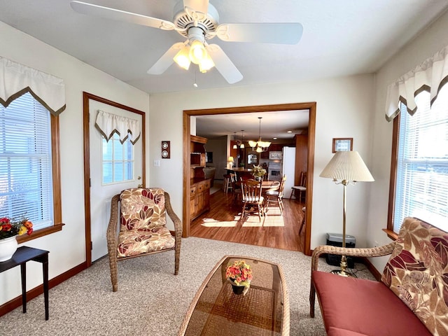 living room featuring ceiling fan with notable chandelier, baseboards, and wood finished floors