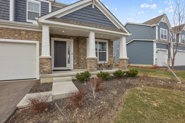 view of front facade featuring covered porch, stone siding, aphalt driveway, and a garage