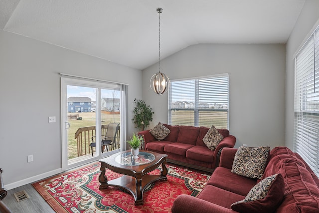 living room featuring plenty of natural light, wood finished floors, visible vents, and a notable chandelier