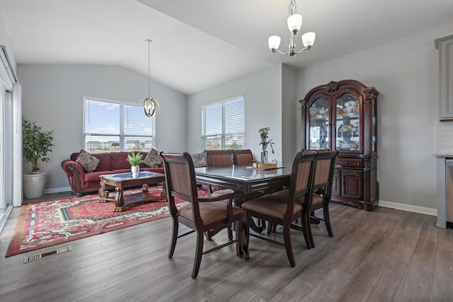 dining space with baseboards, a chandelier, vaulted ceiling, and wood finished floors