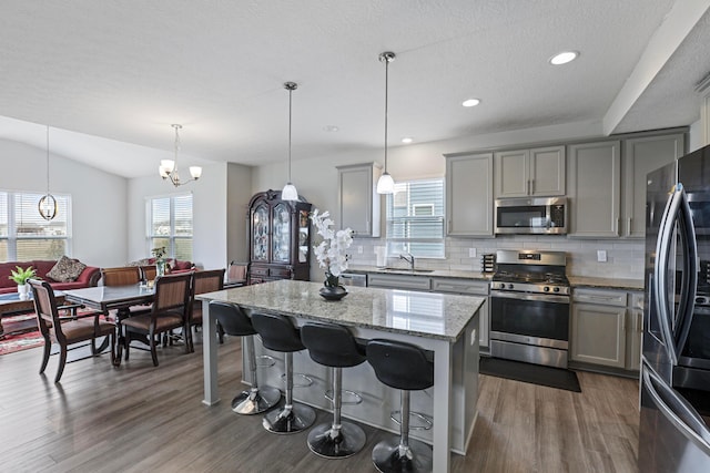 kitchen with light stone counters, a center island, stainless steel appliances, gray cabinetry, and a wealth of natural light