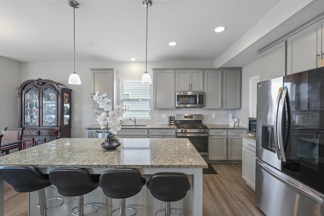 kitchen featuring gray cabinetry, a sink, wood finished floors, appliances with stainless steel finishes, and decorative backsplash