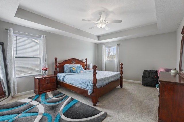 carpeted bedroom featuring baseboards, a tray ceiling, and a ceiling fan