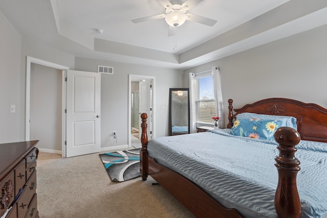 bedroom featuring a tray ceiling, light colored carpet, visible vents, ceiling fan, and baseboards