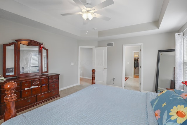 carpeted bedroom with a ceiling fan, baseboards, visible vents, and a tray ceiling