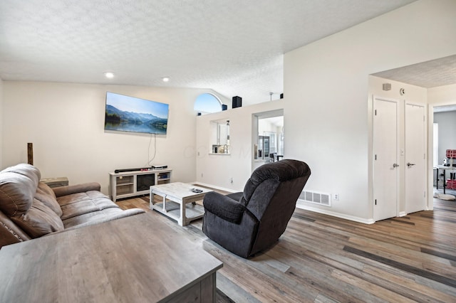 living area with vaulted ceiling, a textured ceiling, wood finished floors, and visible vents