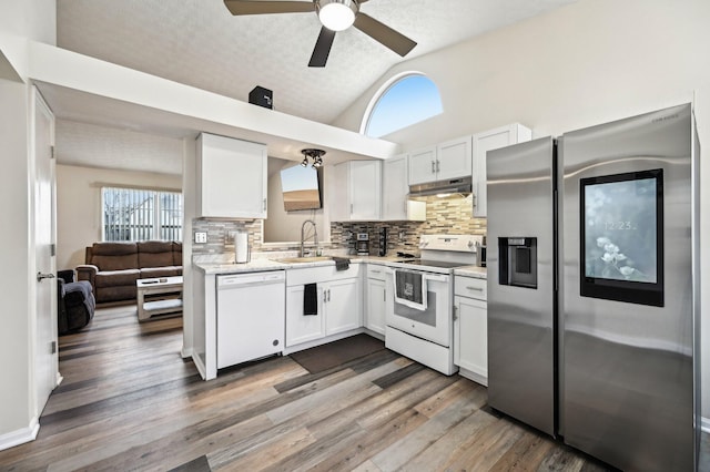 kitchen featuring white appliances, lofted ceiling, light countertops, under cabinet range hood, and a sink