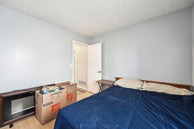 bedroom with light wood-type flooring, visible vents, and a textured ceiling