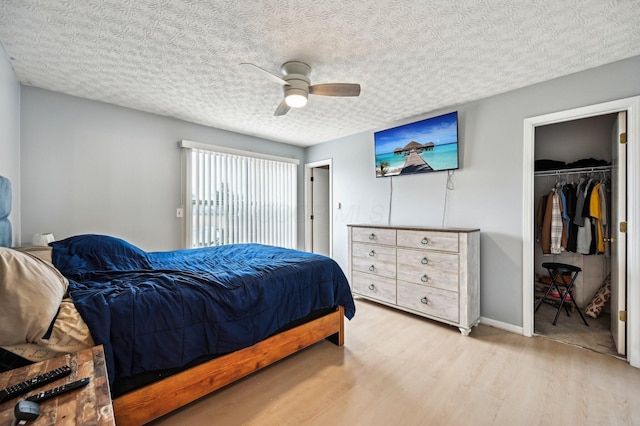 bedroom featuring a textured ceiling, a ceiling fan, baseboards, a closet, and light wood-type flooring