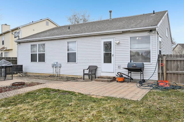 back of house with entry steps, a patio, a shingled roof, fence, and a yard