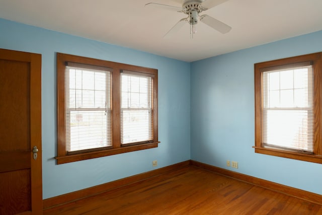 spare room with baseboards, wood finished floors, a ceiling fan, and a healthy amount of sunlight