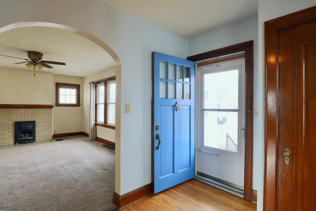 foyer featuring arched walkways, ceiling fan, baseboards, and light colored carpet