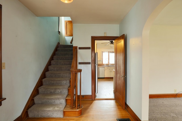 stairway with arched walkways, baseboards, and wood finished floors