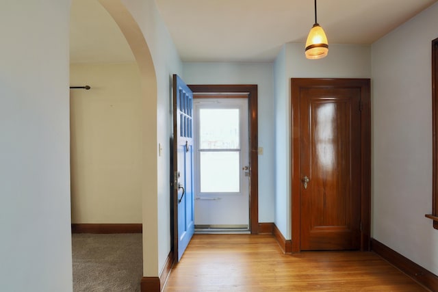 entryway featuring arched walkways, baseboards, and light wood-style floors