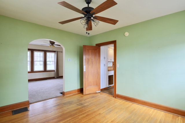 spare room with arched walkways, visible vents, light wood-style flooring, ceiling fan, and baseboards