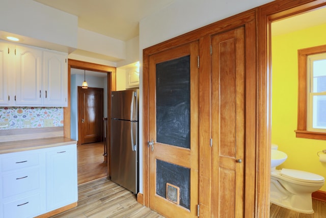 kitchen featuring light countertops, light wood-type flooring, freestanding refrigerator, and white cabinets