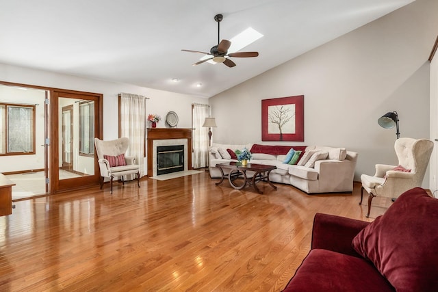 living area featuring ceiling fan, high vaulted ceiling, light wood finished floors, and a fireplace