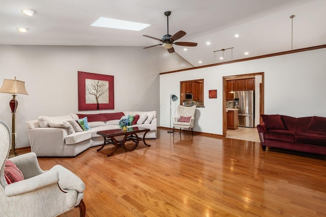 living area with recessed lighting, a ceiling fan, light wood-type flooring, vaulted ceiling with skylight, and baseboards