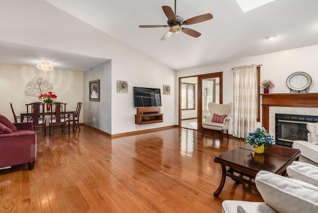 living room with lofted ceiling, ceiling fan, wood finished floors, baseboards, and a tiled fireplace