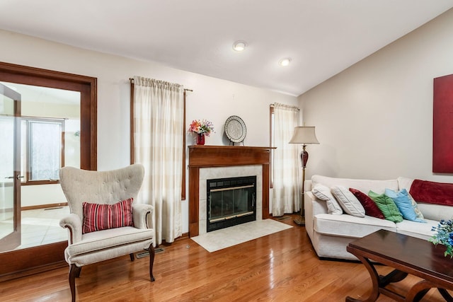 living room featuring visible vents, vaulted ceiling, a tiled fireplace, and wood finished floors