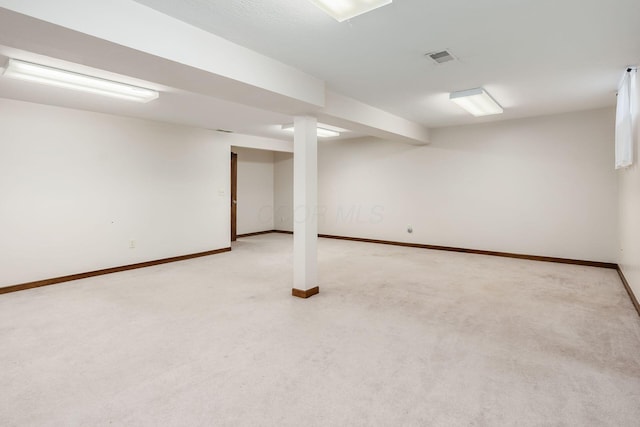 finished basement with baseboards, visible vents, and light colored carpet