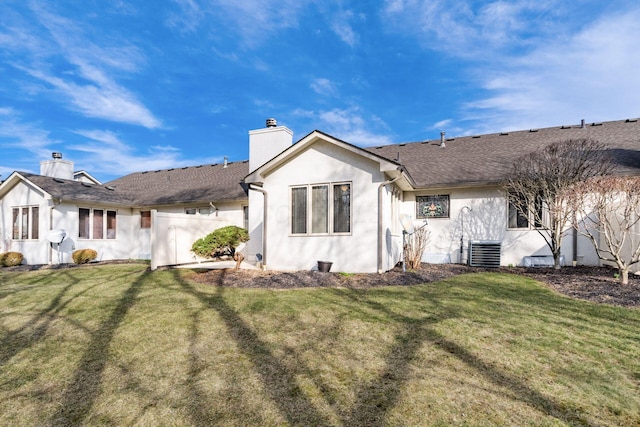 rear view of property featuring roof with shingles, a chimney, stucco siding, a lawn, and central AC unit