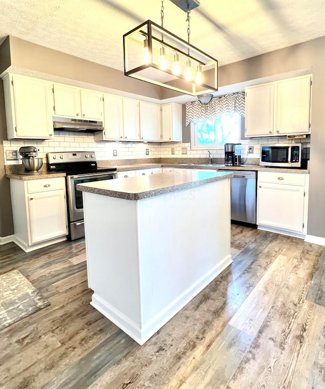 kitchen featuring tasteful backsplash, a kitchen island, under cabinet range hood, stainless steel appliances, and dark wood-style flooring