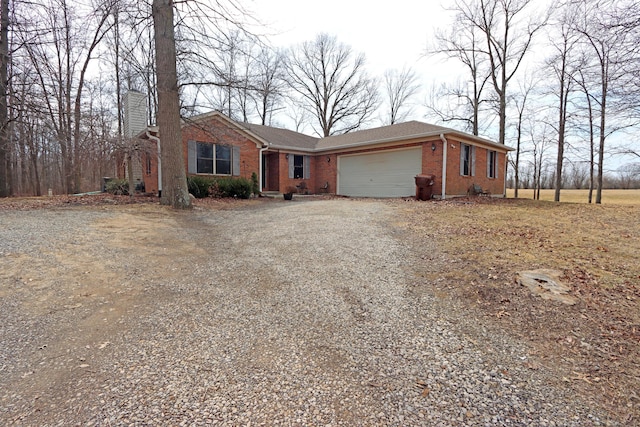 ranch-style house with gravel driveway, brick siding, a chimney, and an attached garage