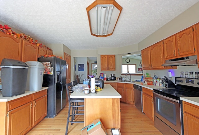 kitchen featuring light wood-style flooring, appliances with stainless steel finishes, a center island, under cabinet range hood, and a sink