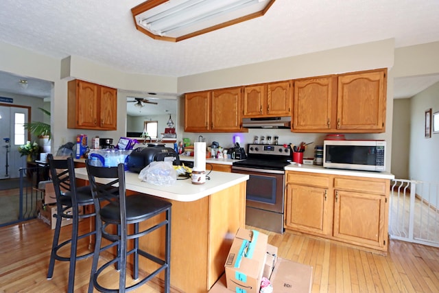 kitchen with light wood finished floors, a breakfast bar area, stainless steel appliances, light countertops, and under cabinet range hood