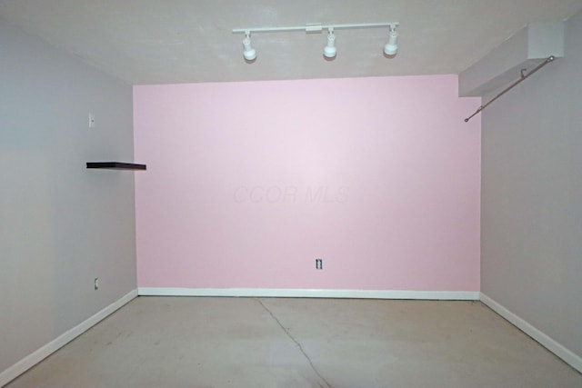 spare room featuring concrete floors, baseboards, and track lighting