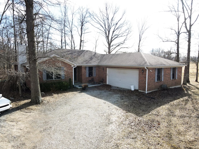 ranch-style house featuring gravel driveway, an attached garage, roof with shingles, and brick siding