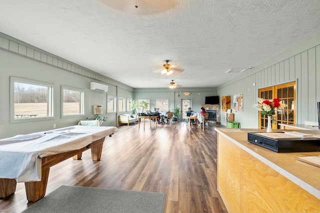 rec room featuring a ceiling fan, an AC wall unit, a textured ceiling, wood finished floors, and billiards