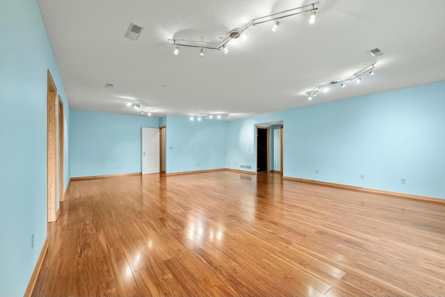 empty room featuring track lighting, light wood-type flooring, visible vents, and baseboards