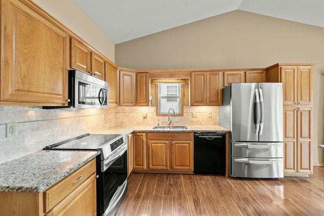 kitchen with lofted ceiling, light stone counters, stainless steel appliances, light wood-style floors, and a sink