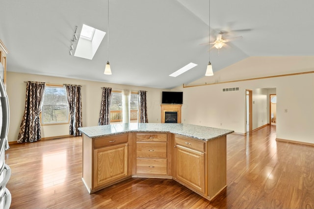 kitchen featuring vaulted ceiling with skylight, visible vents, open floor plan, light wood finished floors, and a glass covered fireplace