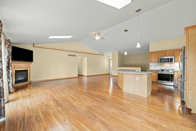 kitchen with vaulted ceiling with skylight, stainless steel appliances, open floor plan, light countertops, and a glass covered fireplace