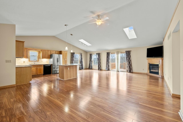 unfurnished living room featuring lofted ceiling with skylight, a glass covered fireplace, a sink, and wood finished floors