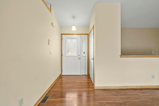 doorway featuring lofted ceiling, visible vents, baseboards, and wood finished floors