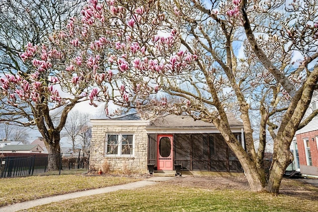 view of front facade with stone siding, a front lawn, fence, and a sunroom